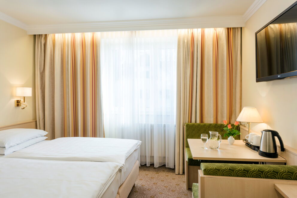 Helles Doppelzimmer mit Tisch, TV und Wasserkocher, gemeinsam mit elegantem Vorhang.