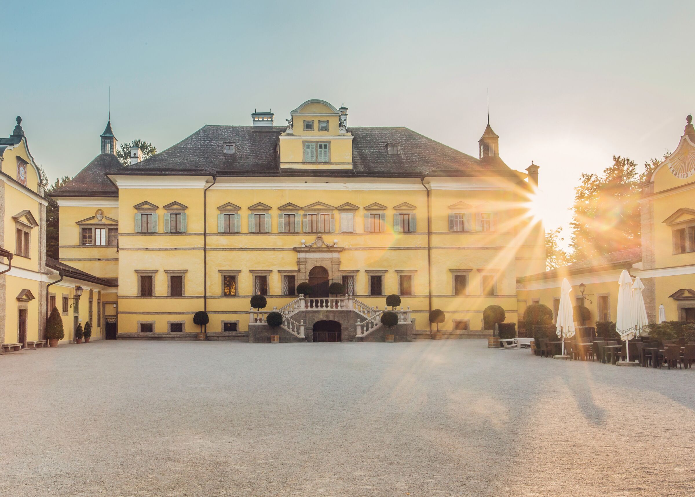 Das Schloss Hellbrunn in Salzburg von vorne, während die Sonne hinter bei hervorscheint in den Innenhof © Tourismus Salzburg