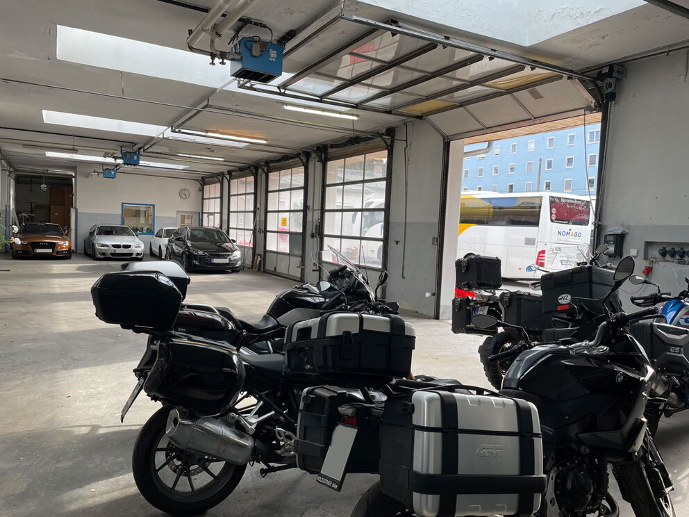 Motorräder und Autos in einer geräumigen Garage mit natürlichem Licht.