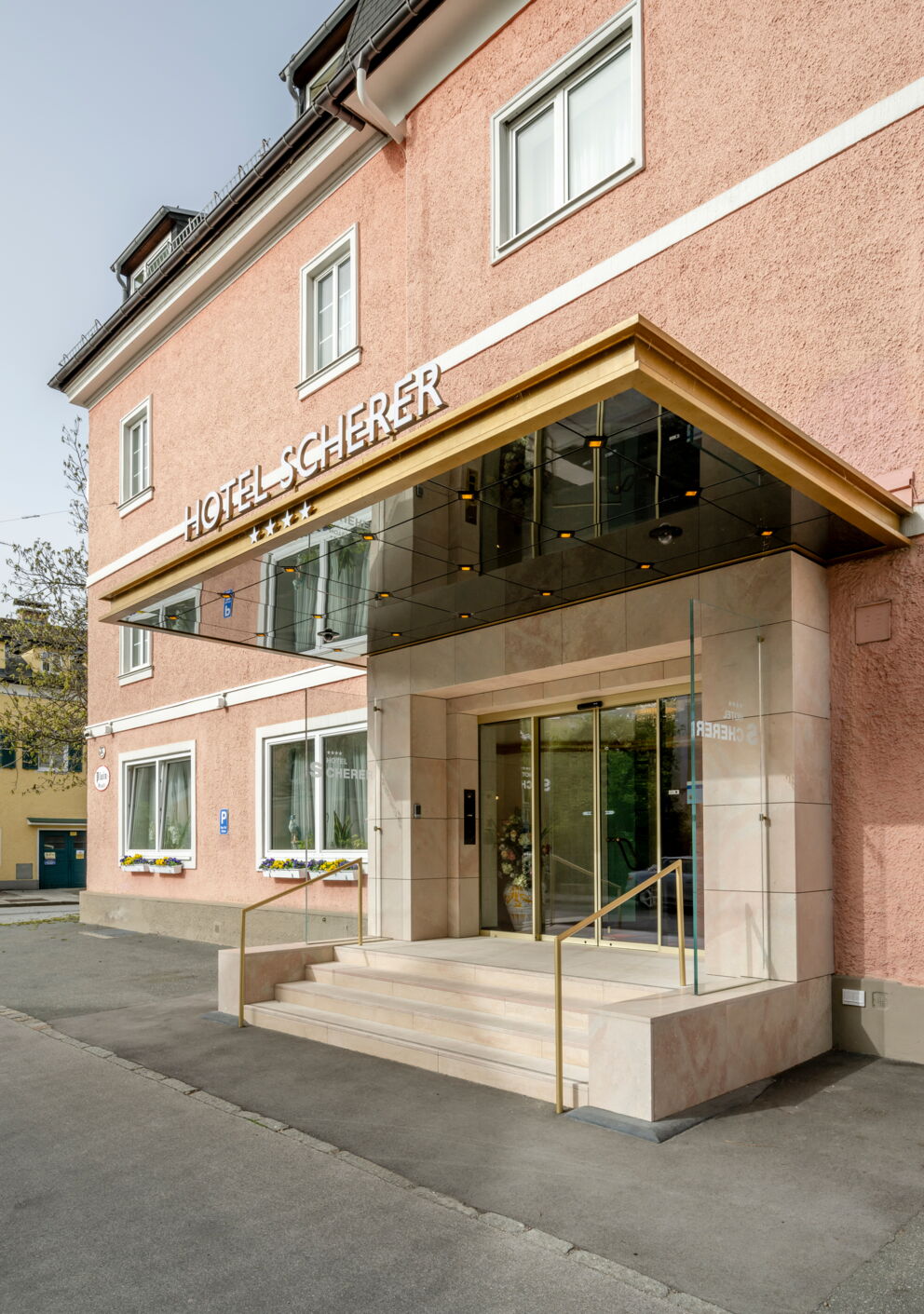 Inviting entrance to Hotel Scherer with glass canopy and flower arrangement.