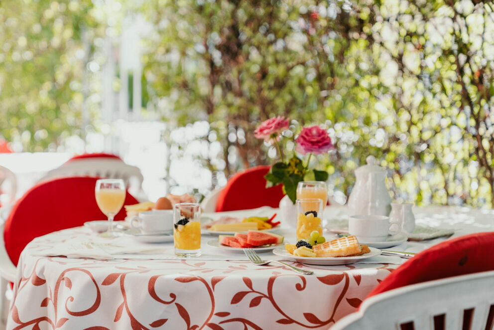 Frühstückstisch im Freien mit frischen Säften, Gebäck und Blumenarrangement.