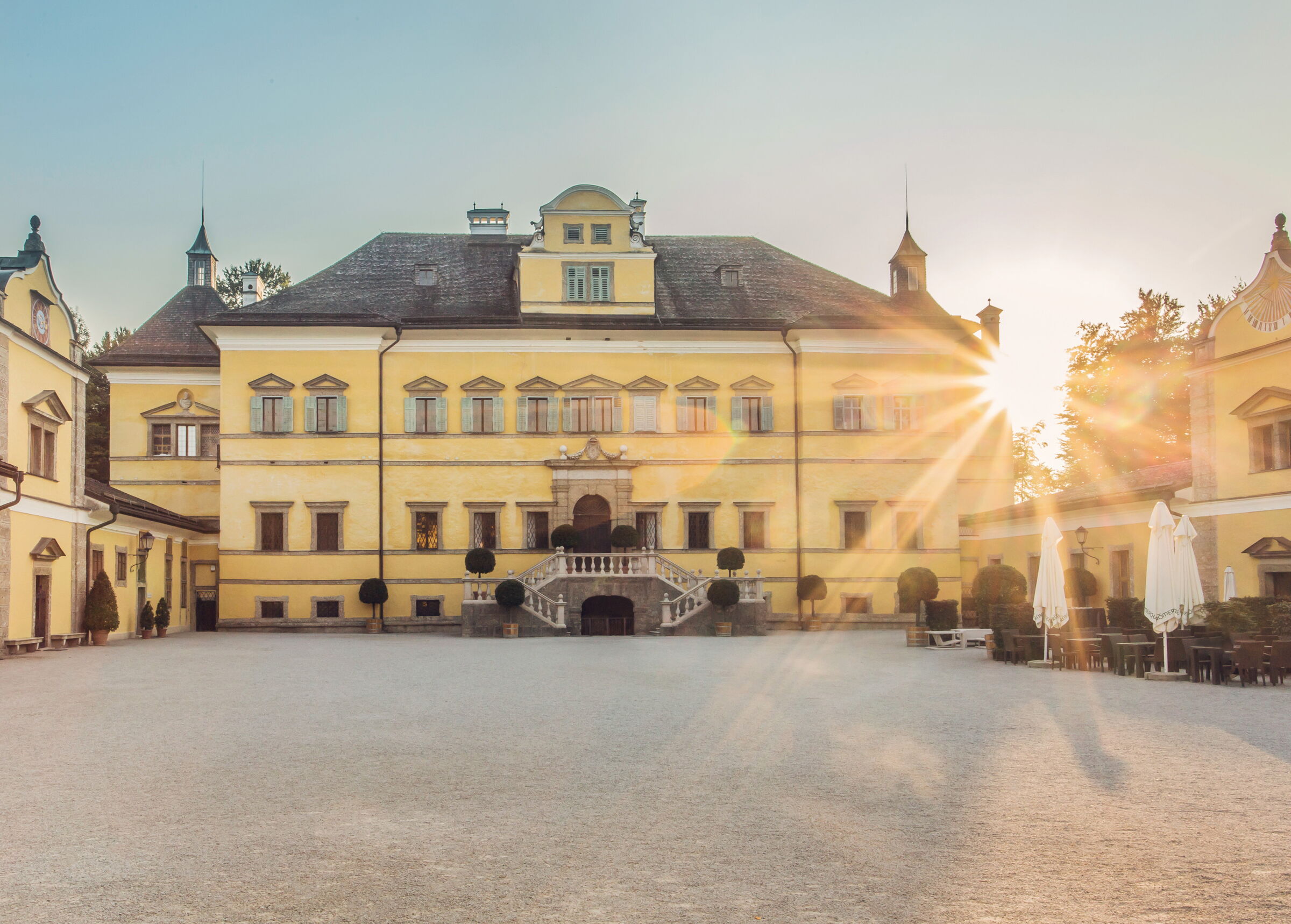 Hellbrunn Palace in Salzburg from the front, while the sun shines behind it into the inner courtyard © Tourismus Salzburg