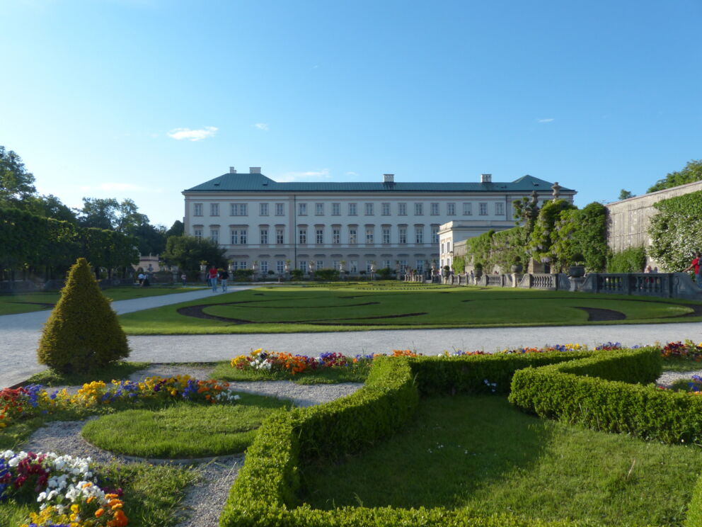 Magnificent baroque garden with blooming flowers and imposing building in the background.