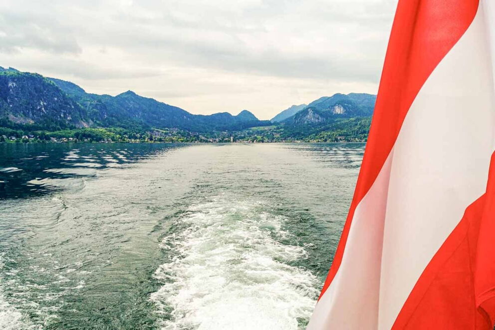 View of picturesque lake with Austrian flag and surrounding mountains.