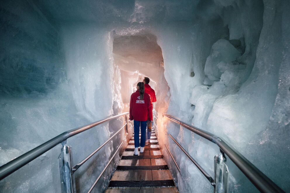 People in red jackets explore fascinating ice caves with ice-blue walls.
