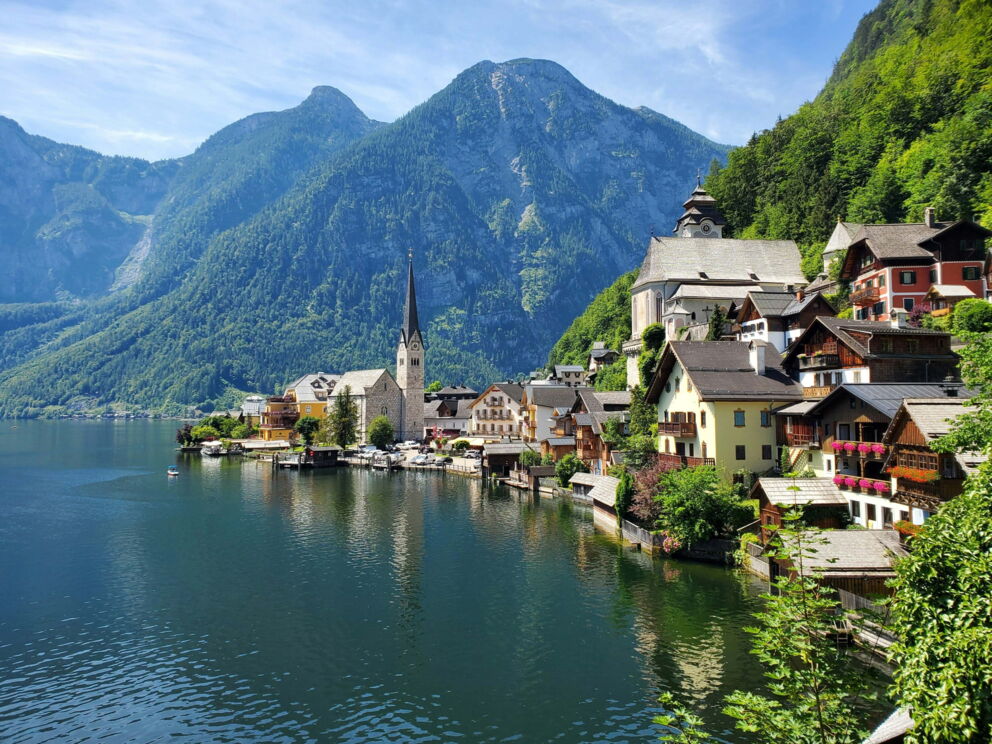 A breathtaking panoramic view of Hallstatt with historic buildings and a church in the foreground, surrounded by green mountains and clear water. © Hasmik Ghazaryan Olson Unsplash