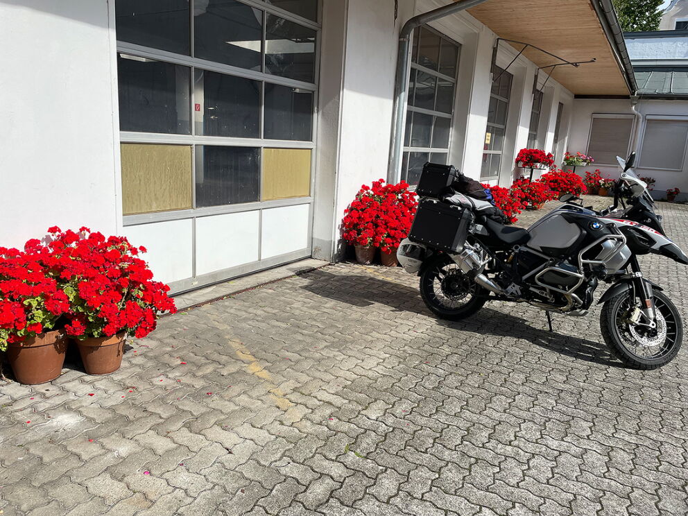 Motorrad geparkt auf Innenhof mit leuchtend roten Blumen und Garagentüren