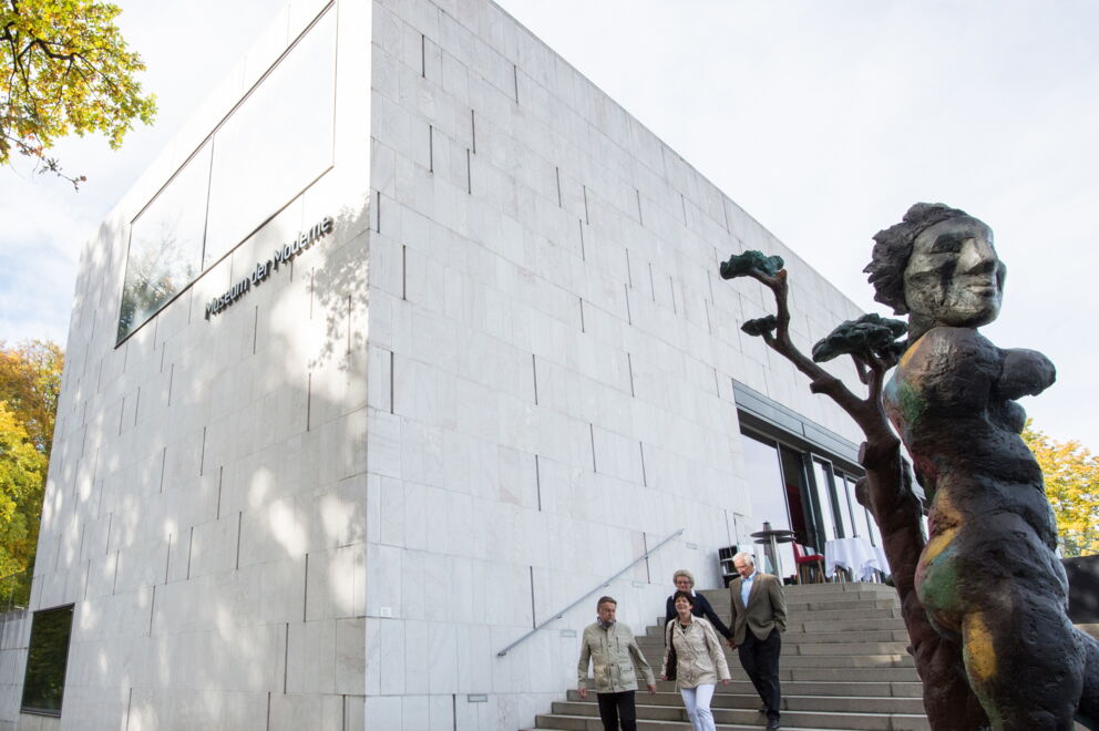 Besucher vor dem modernen Museumseingang mit beeindruckender Skulptur im Vordergrund.