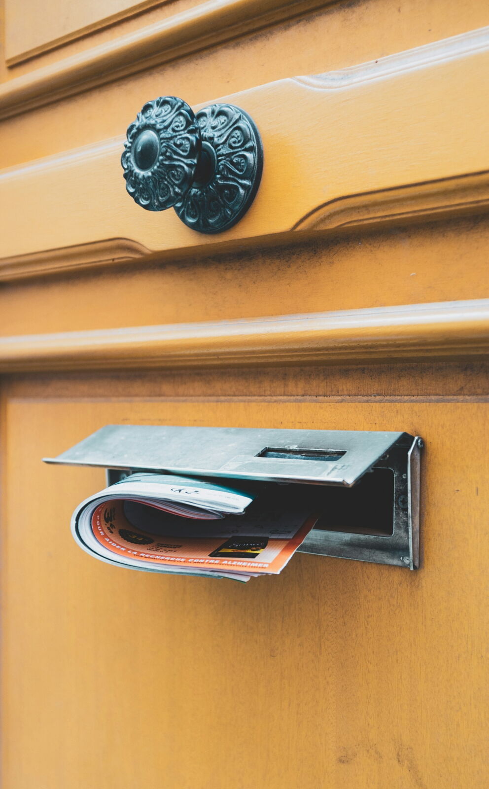 Eine Holztür mit Briefschlitz, durch den eine Zeitung hereingesteckt wurde. ©Mihai Moisa auf Unsplashed