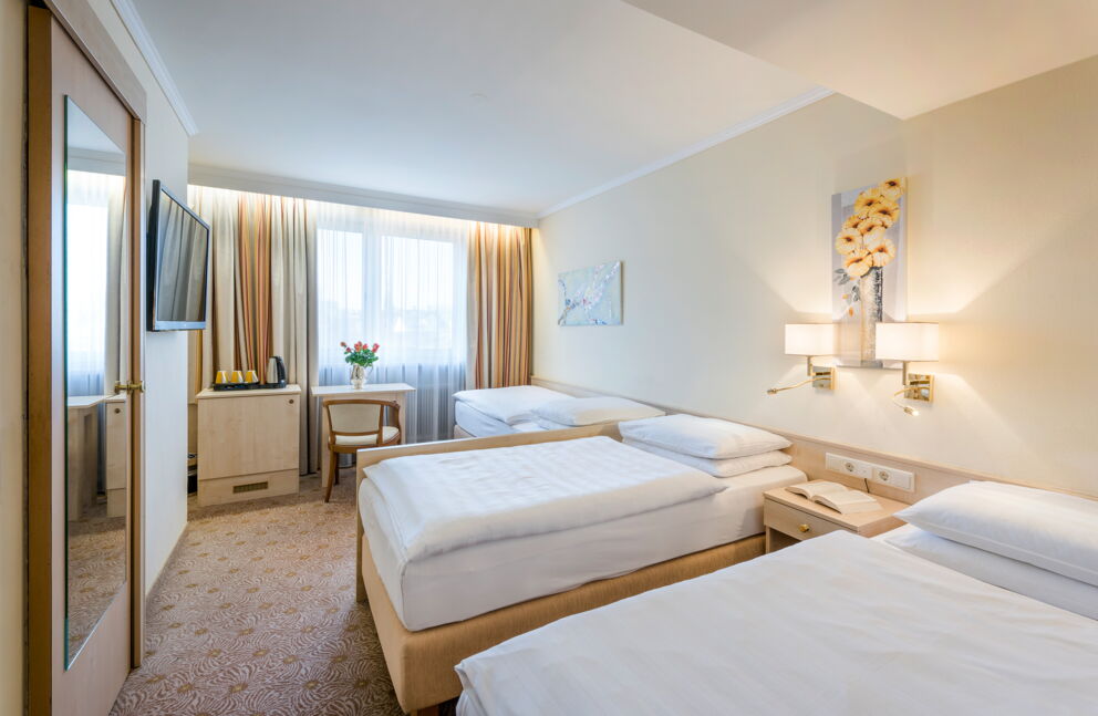 Helles Zimmer mit zwei Betten, gemütlichem Tisch und stilvollen Vorhängen.