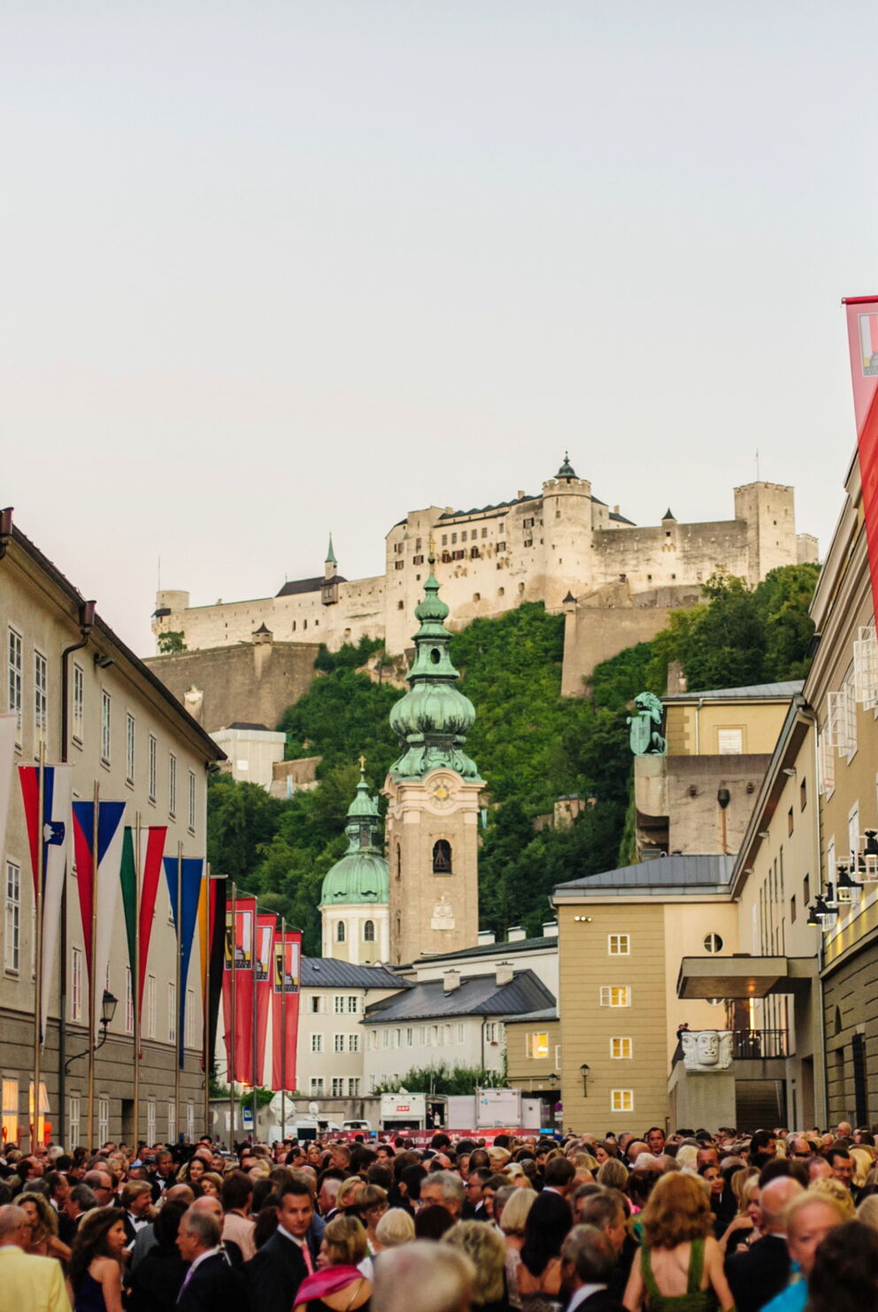 Menschenmenge bei den Salzburger Festspielen, umgeben von historischen Gebäuden und Fahnen.