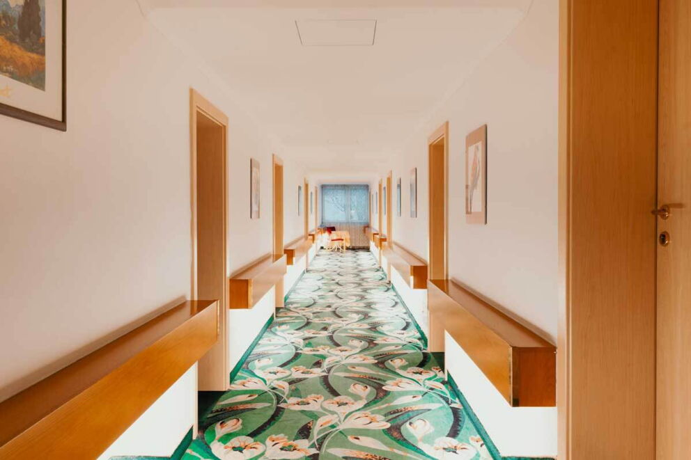 Heller Hotelgang mit grünem, floralem Teppich und mehreren Türen.