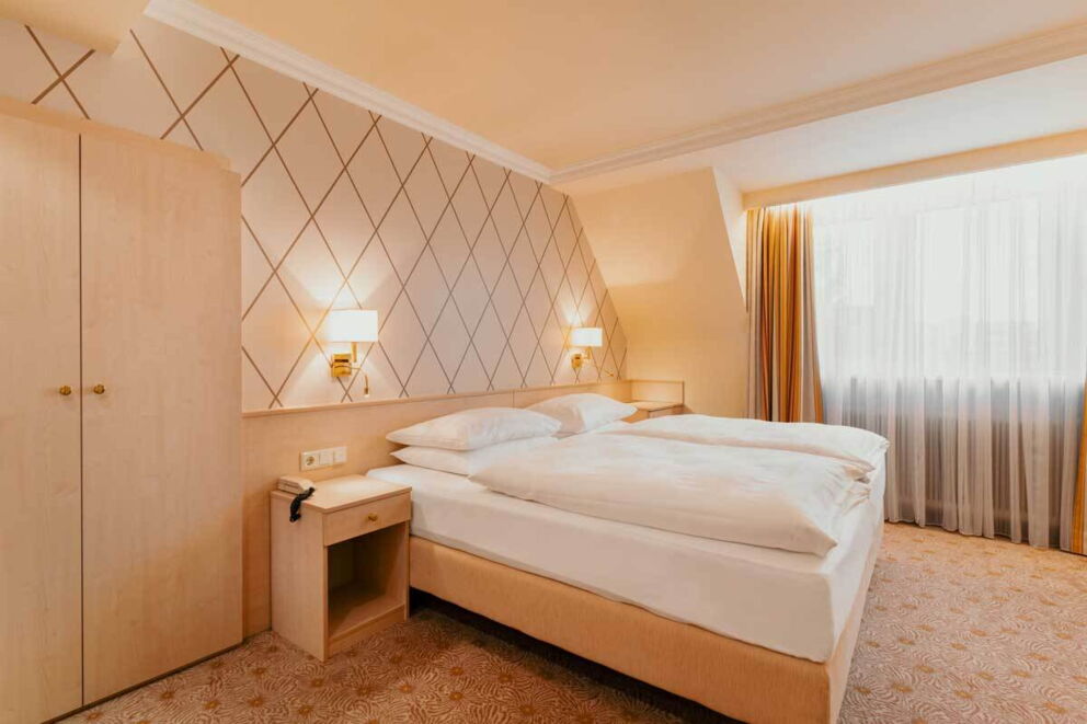 Helles Zimmer mit Doppelbett, stilvollen Lampen und modernem Teppichboden.