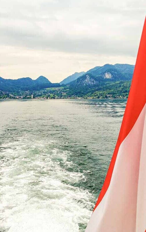 Bootsfahrt mit österreichischer Flagge, umgeben von majestätischen Alpen und See.