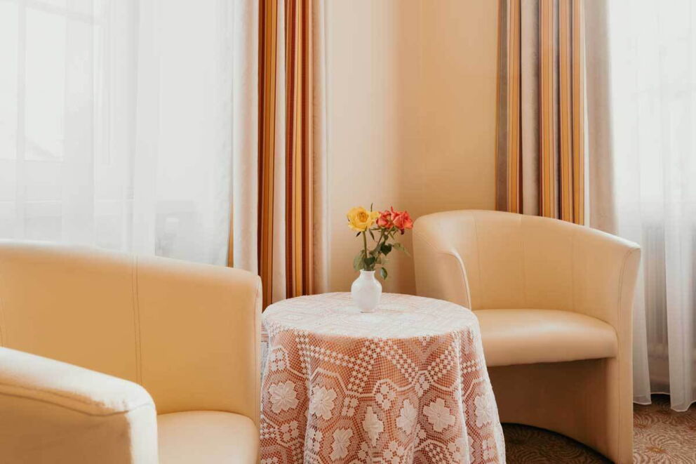 Zwei beige Sessel mit Tisch und Blumen.