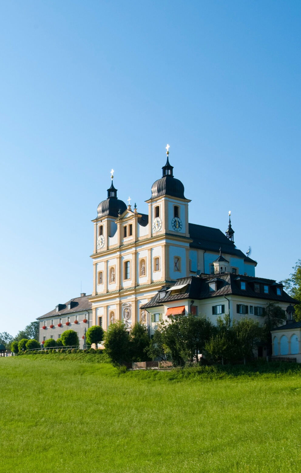 Barockes Gebäude auf grüner Wiese unter klarem, blauem Himmel in der Sonne.