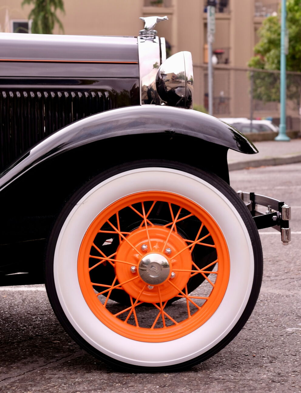 Vintage car wheel with orange spokes and white tires on a grey road.