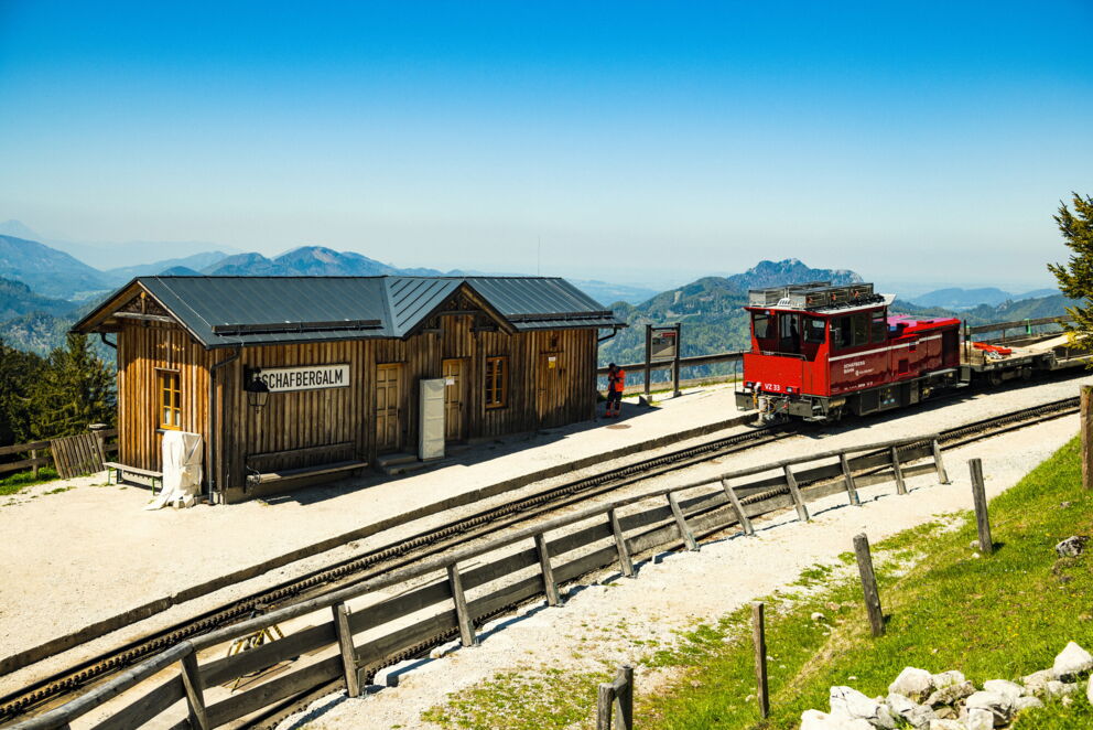 Red cable car in front of a wooden hut on the Schafbergalm with an impressive mountain panorama.