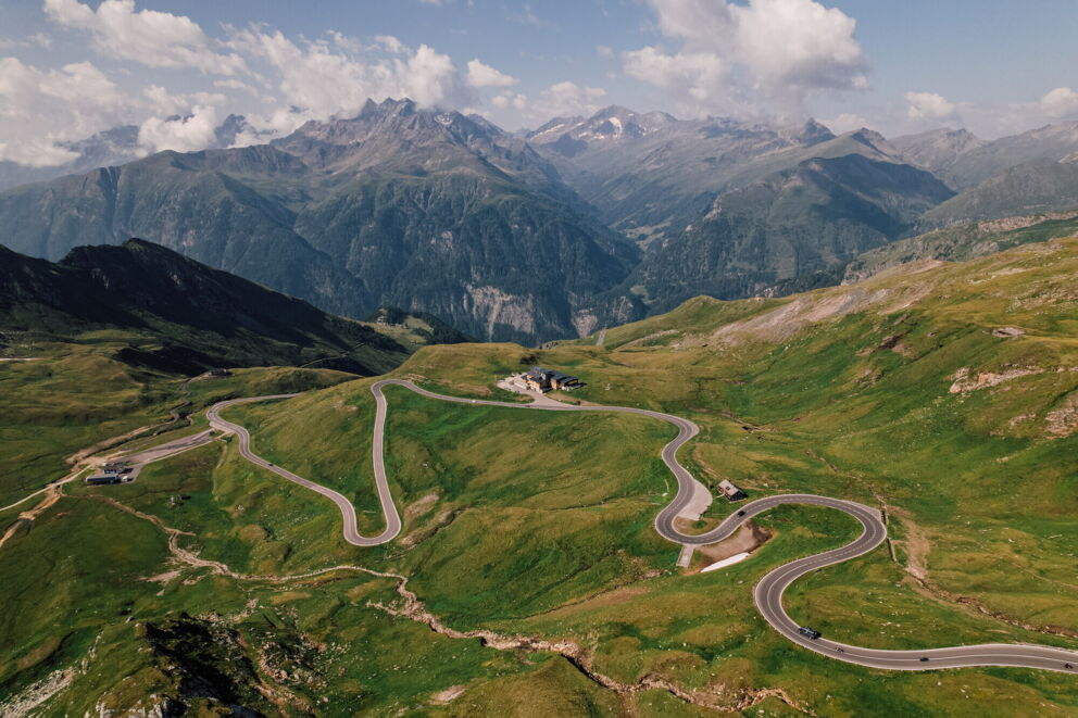 Winding road through a green mountain landscape with an impressive Alpine panorama in the background.