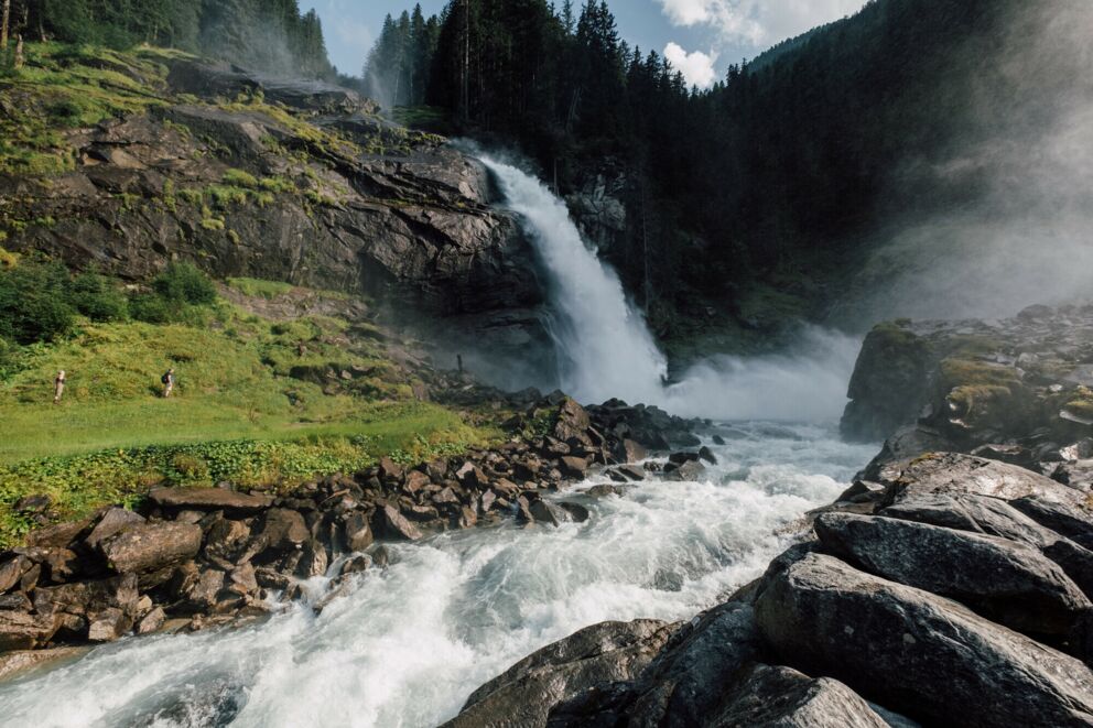 Roaring waterfall in the midst of a lush, green landscape and dense forests.