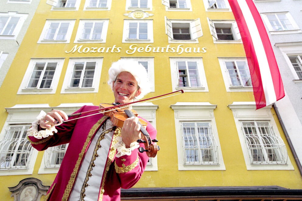 Mann in historischer Kleidung spielt Geige vor Mozarts Geburtshaus in Salzburg.