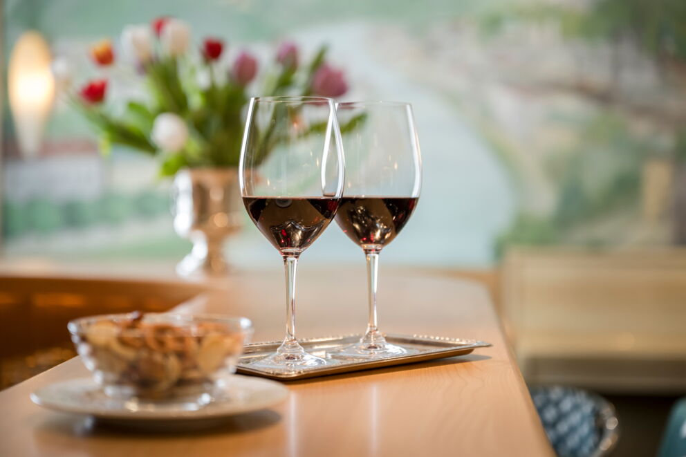 Two glasses of red wine on a wooden table with flowers in the background