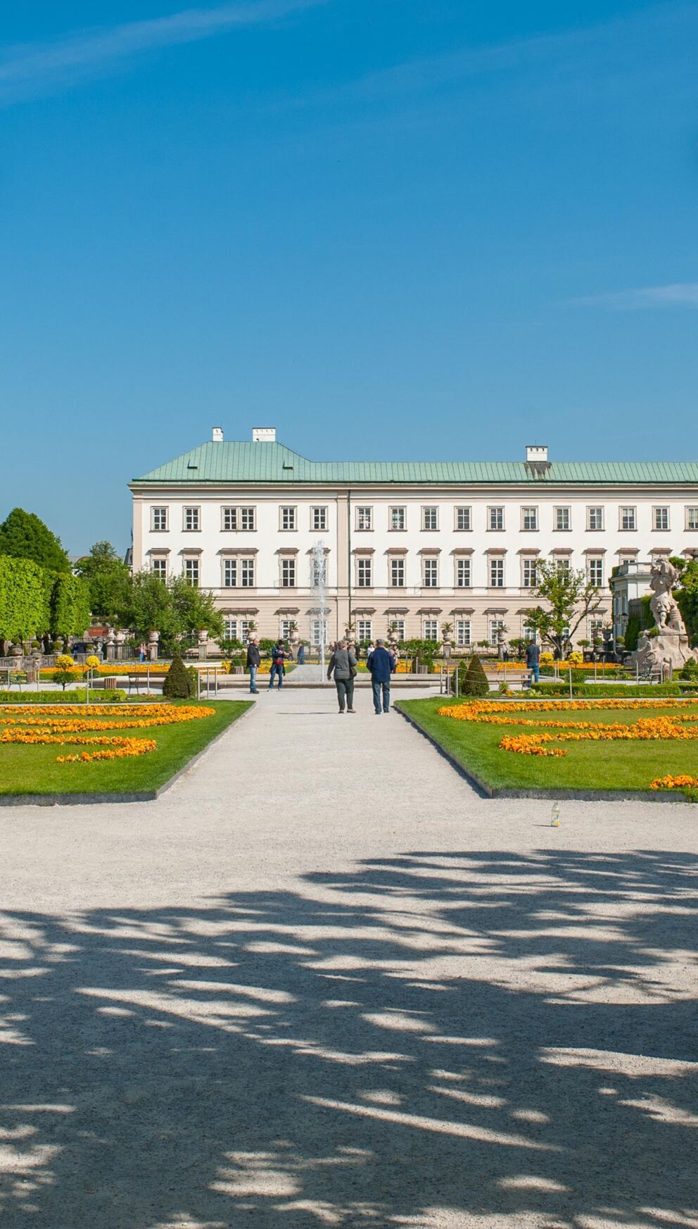 Elegant sculptures in Mirabell Gardens with the palace building in the background in sunny weather.