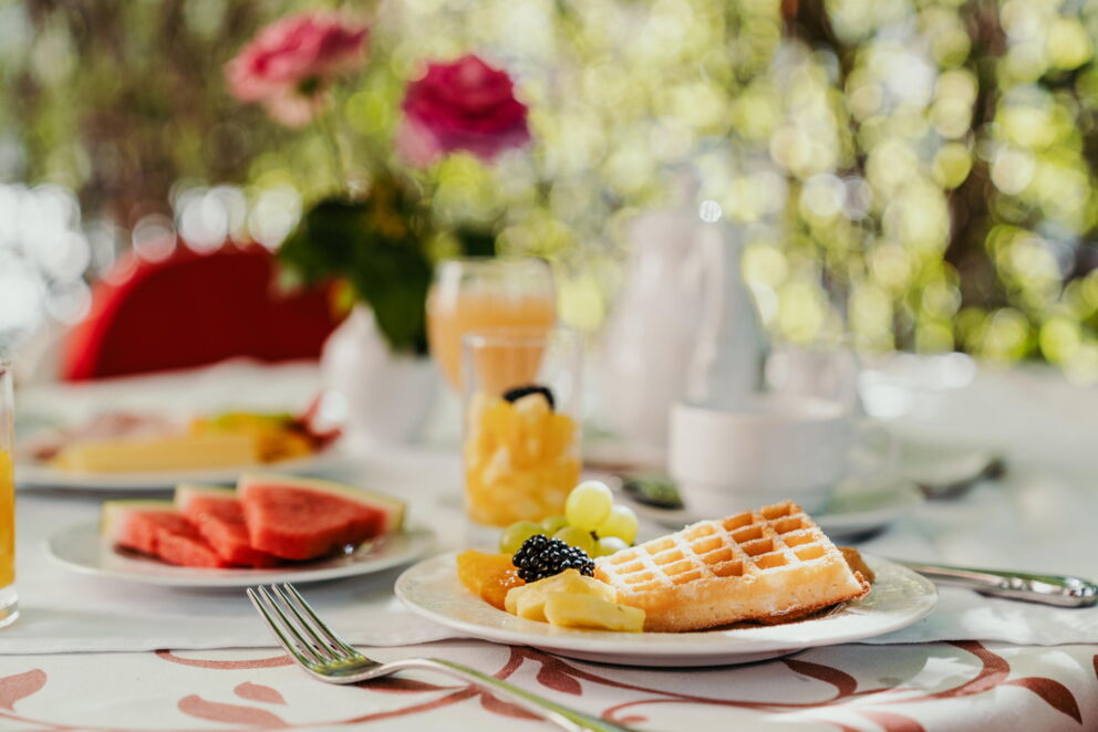 Frisches Frühstück mit Waffeln, Obst und Orangensaft auf blumengeschmücktem Tisch.