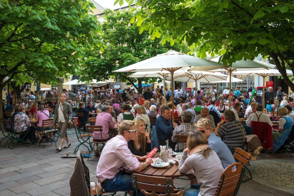 Menschen genießen unter grünen Bäumen das gesellige Beisammensein in einem belebten Biergarten.