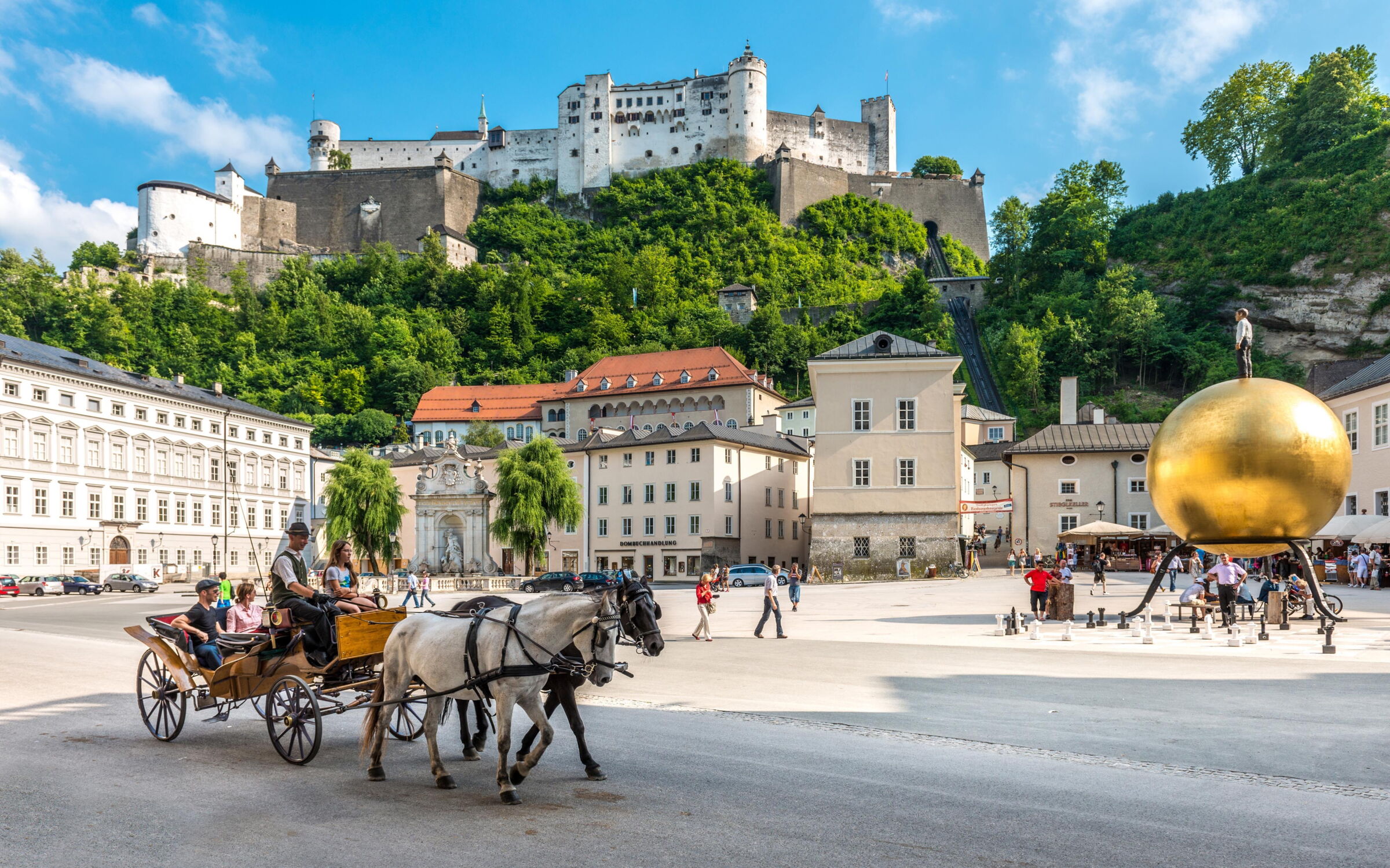 Kapitalplatz with a passing horse-drawn carriage and the fortress in the background on a sunny day in Salzburg © Tourismus Salzburg