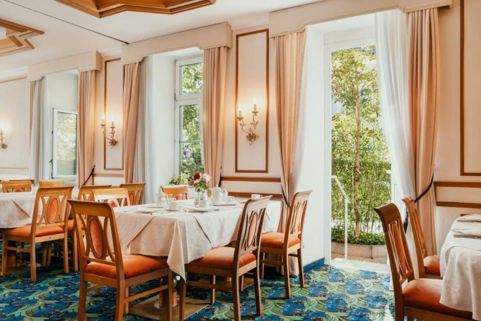 Heller, traditioneller Speisesaal mit gedeckten Tischen und Blick ins Grüne
