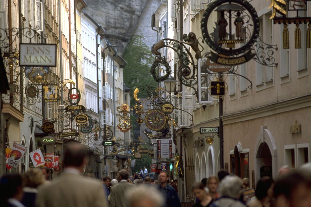 Menschen schlendern durch eine historische Gasse in Salzburg mit zahlreichen Schildern.