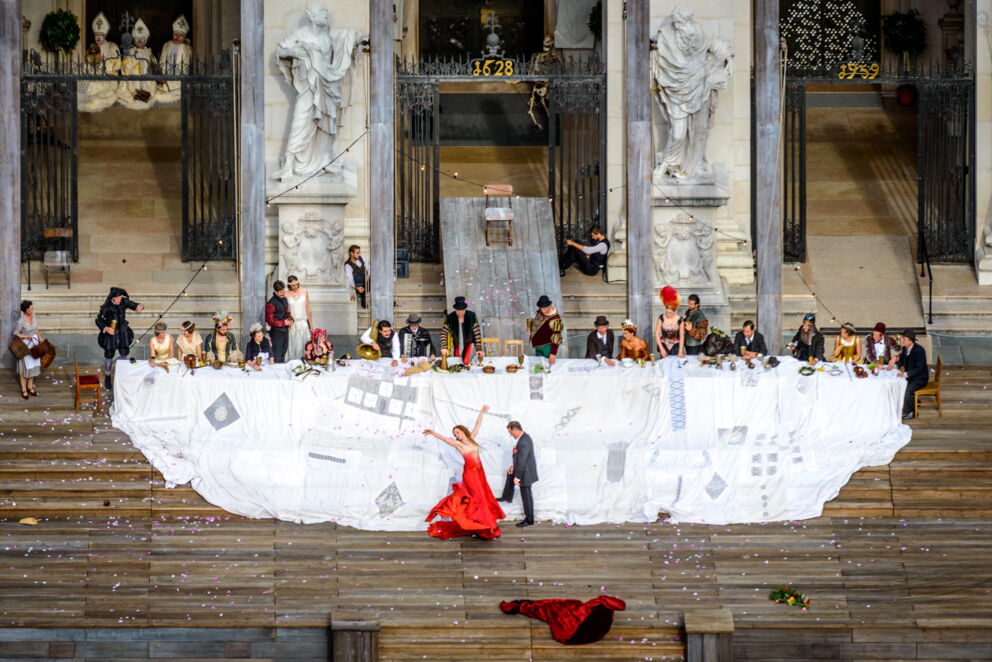 People in historical costumes at a long table in front of impressive architecture.