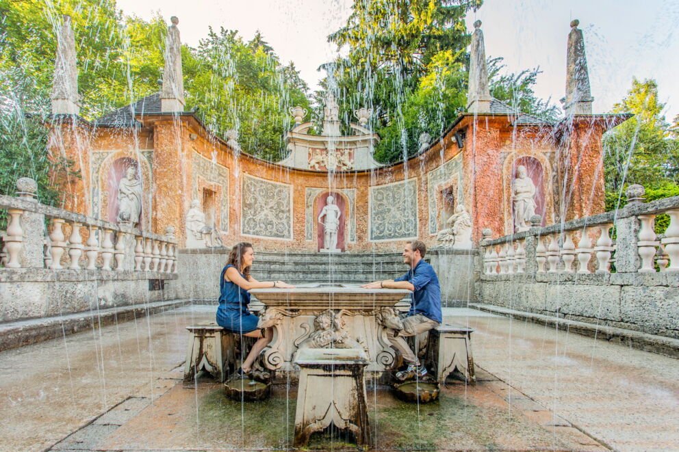 People at a table, surrounded by a historic fountain and water features.