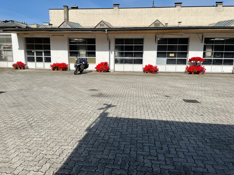 Motorrad parkt auf gepflastertem Hof mit roten Blumen in Töpfen.
