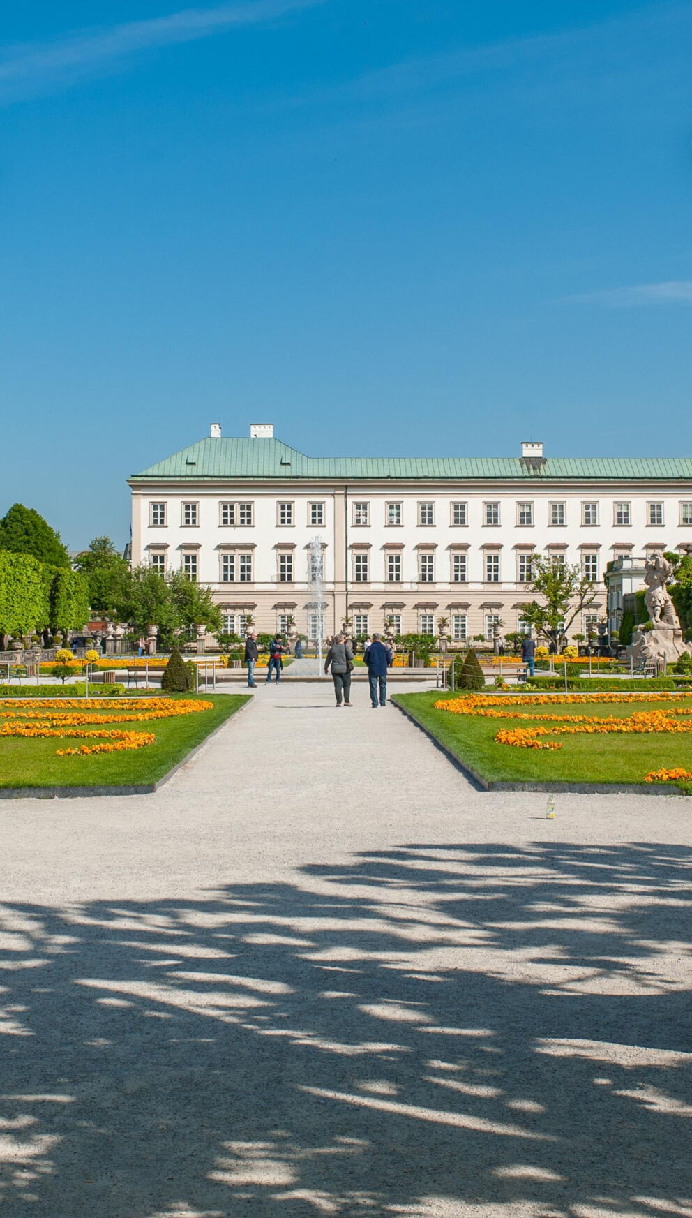 Elegant sculptures in Mirabell Gardens with the palace building in the background in sunny weather.
