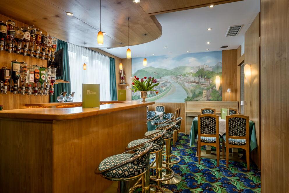 Elegante Bar mit Holztheke, stilvollen Hockern und Wandbild in warmem Licht.