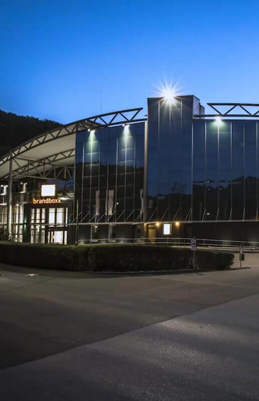 Großes Gebäude mit Glasfassade und eindrucksvoller Beleuchtung am Abendhimmel.