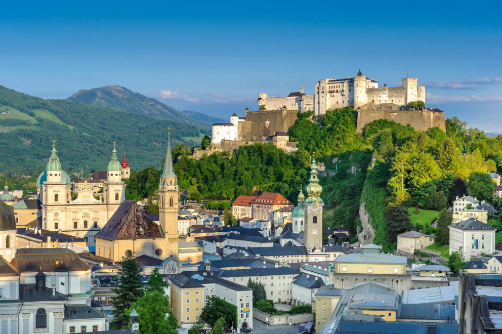 Blick auf Salzburgs historische Altstadt mit Festung und grünen Hügeln im Hintergrund.