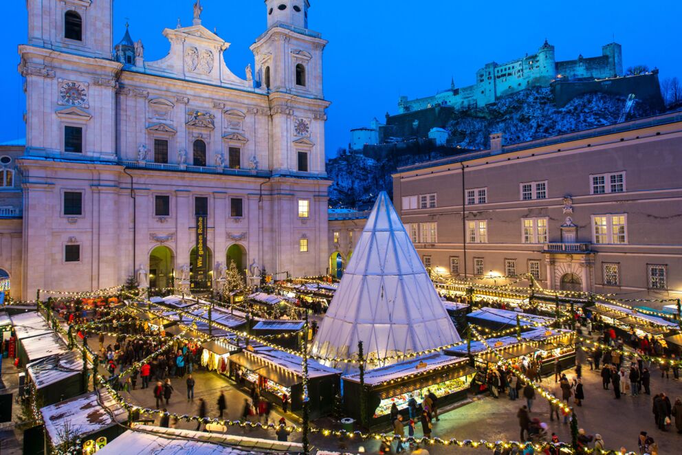 Festlich geschmückter Weihnachtsmarkt mit Lichtern, Ständen und historischer Architektur bei Nacht.