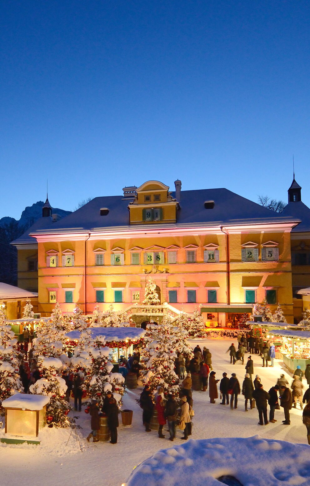 Festlich beleuchteter Weihnachtsmarkt im Innenhof mit Besuchern bei Dämmerung.