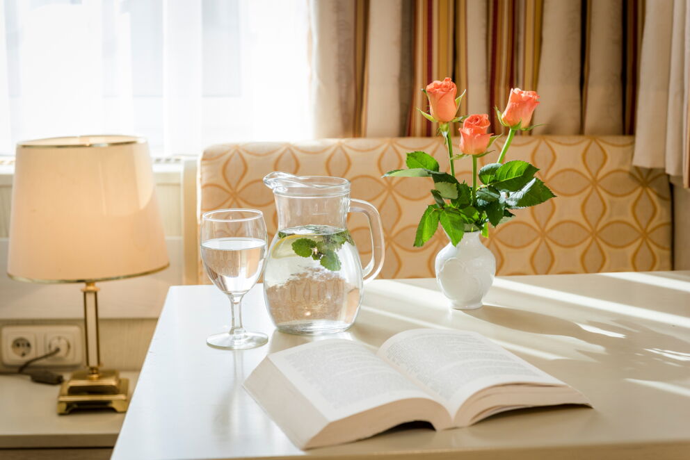 Ein Tisch auf dem ein Buch, ein Krug, ein Glas Wasser und und drei Rosen in einer Vase stehen