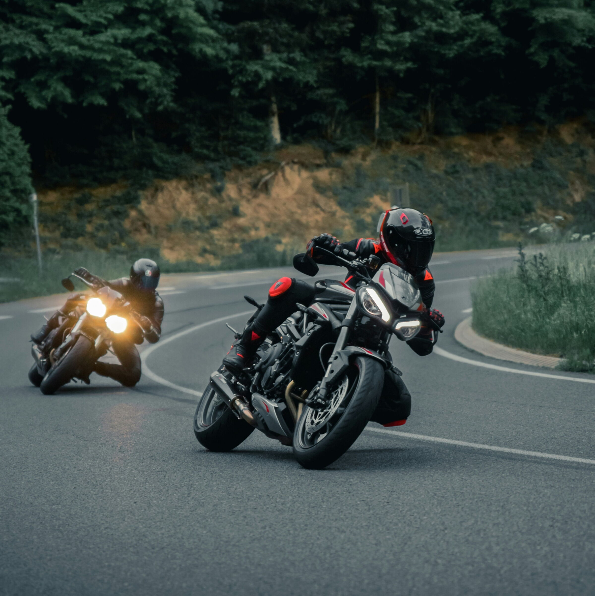 Two motorcyclists on a bend in the open road surrounded by trees.