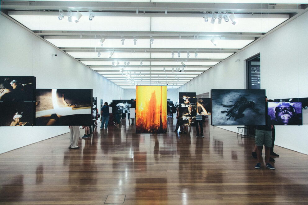 Menschen betrachten Kunstwerke in moderner Galerie mit hellem Licht und Holzboden.