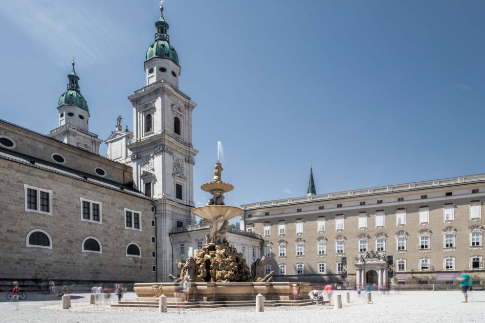 Historic buildings and fountains on Cathedral Square on a sunny day in Salzburg.